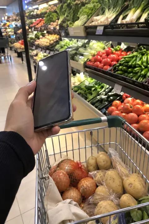 Mano con el móvil en el pasillo de frutas y verduras del súper, junto al carro