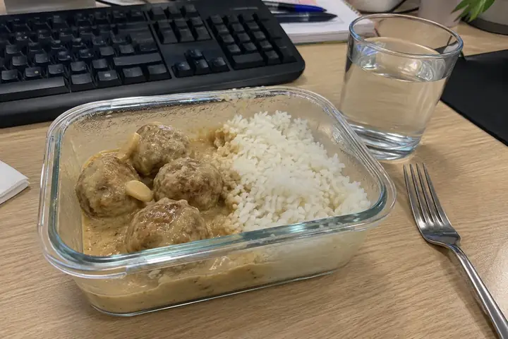 Táper de vidrio abierto con albóndigas y arroz en una mesa de oficina
